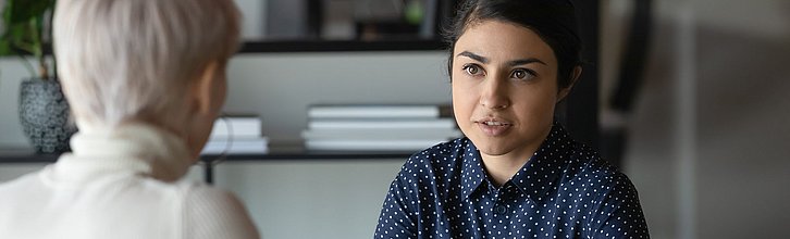 Zwei Personen miteinander im Gespräch, eine Person sieht man nur von hinten